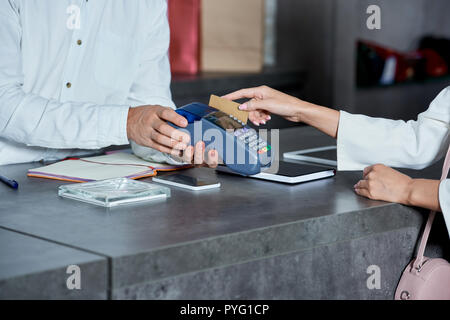 cropped shot of worker holding payment terminal and woman paying with credit card in shop Stock Photo