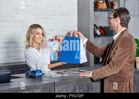 smiling young seller giving shopping bags to handsome customer in store Stock Photo