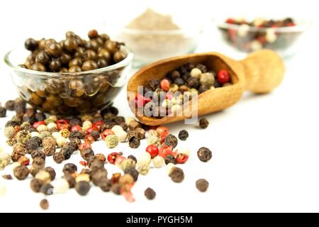 Pepper in wooden spoon. Mix of different peppers balls on white background. Sale of spices Stock Photo