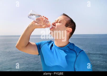 An athlete making a break during training, drinking fresh clean water from a bottle, rests and enjoys the clean air, with a beautiful blue sky. Stock Photo