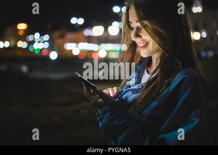 Blogger hipster using in hands gadget mobile phone. Woman pointing finger on blank screen smartphone on background bokeh light in night atmospheric ci Stock Photo