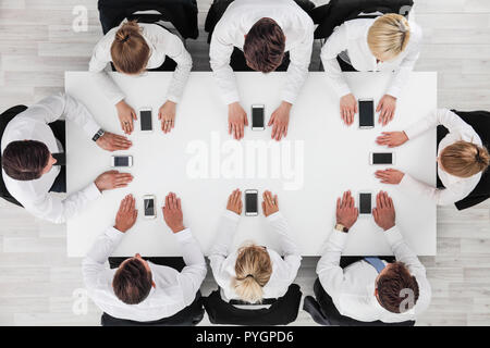 Business people not using smartphones sitting around white table Stock Photo