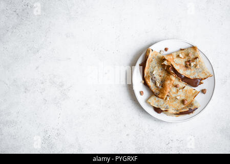 Crepes with chocolate spread and hazelnuts. Homemade thin crepes for breakfast or dessert on white, copy space. Stock Photo