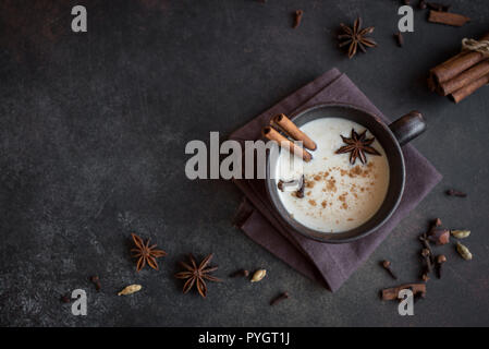 Traditional indian masala chai tea in ceramic cup with ingredients. Spicy black tea with milk on rustic dark background, copy space Stock Photo