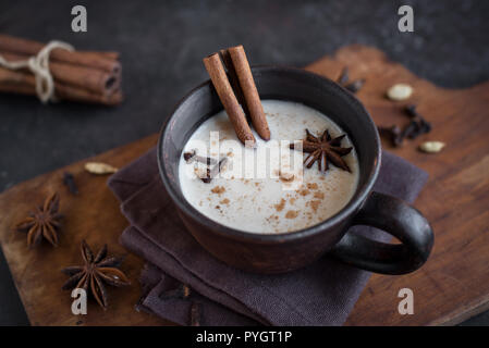 Traditional indian masala chai tea in ceramic cup with ingredients. Spicy black tea with milk on rustic dark background, close up. Stock Photo