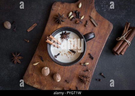 Traditional indian masala chai tea in ceramic cup with ingredients. Spicy black tea with milk on rustic dark background, top view. Stock Photo