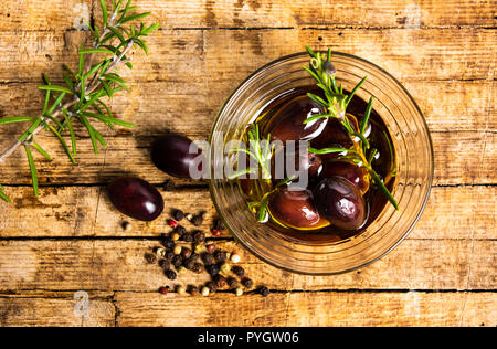 Olives in oil and rosemary on a wooden table top view Stock Photo