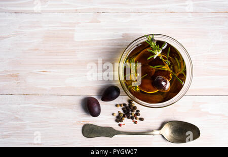 Olives in oil and rosemary on a wooden table top view Stock Photo