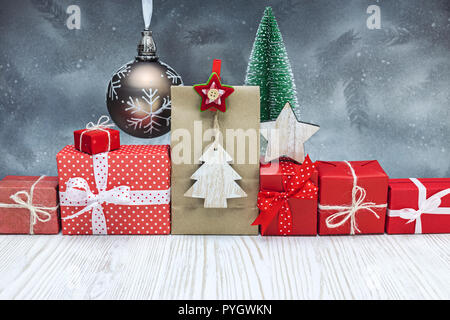 handmade gift boxes wrapped in red paper, decorative glass ball with small christmas tree on festive silver background Stock Photo