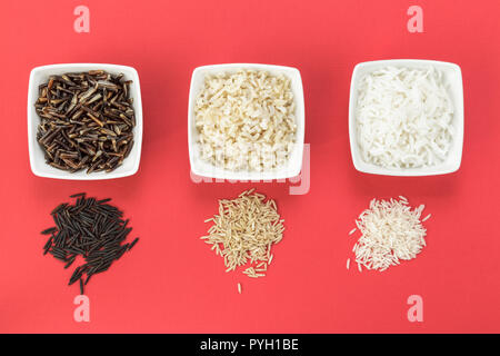 Cooked and uncooked wild, brown and white rice on red background Stock Photo