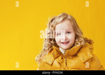 Portrait happy little girl preschooler in a winter jacket. Yellow on a yellow background. Stock Photo