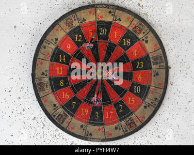 front view of an old casino dart board with american flag arrows on used white wall with holes Stock Photo