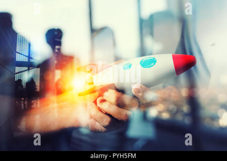 Businessman launches his startup company. Hand holding a wooden rocket. double exposure with light effects Stock Photo