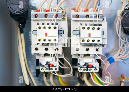 Two electric relays are connected by wires to the metal background. Stock Photo