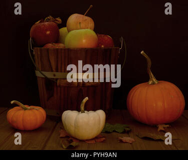 Bucket of assorted apples against black background on wooden table decorated with orange and white pumpkins and a few fall leaves- fall composition Stock Photo