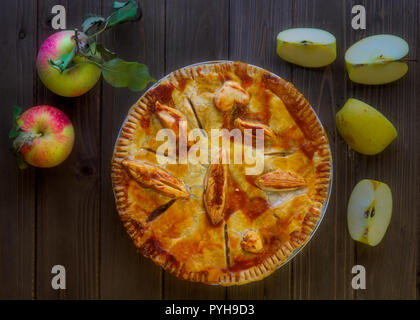 Apple pie decorated with dough leaves on green dishcloth over wooden table, viewed from the top and decorated with whole and halved apples -harvest fo Stock Photo
