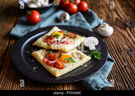 Savory puff pastry pies with egg, bacon, mushrooms and tomato Stock Photo