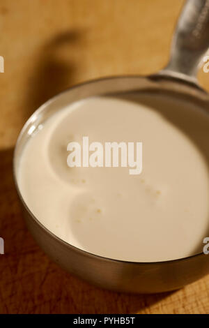 about 3/4 of a cup of American heavy cream in a steel measuring cup. Stock Photo