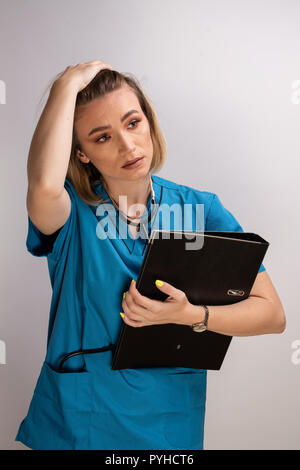 Portrait of tired female doctor holding documents holding hand on the head. Displaying fatigue and many hours spent Stock Photo