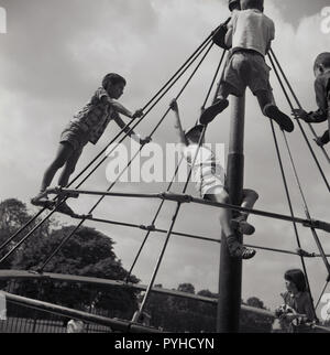 1960s, historical, children playing outside at a playground on a 'Witch's Hat', a piece of metal equipment that was like a roundabout pivoted at the top so as well as going round, it could also sway from side to side. Dangerous..perhaps, but as this picture shows, children, especially boys, loved it! Stock Photo