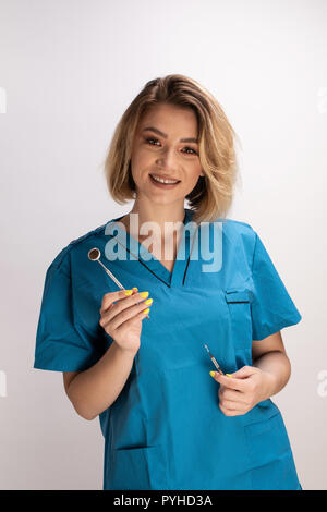 Female dentist holding a mirror and dental tools. Confident smiling professional Stock Photo