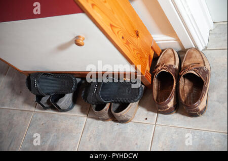 Collection of footwear around and under a shoe cupboard. Stock Photo