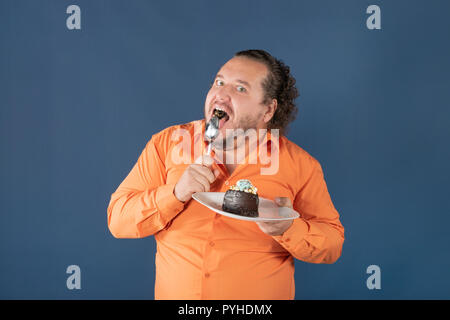 Funny fat man in orange shirt with a piece of chocolate cake on a plate Stock Photo