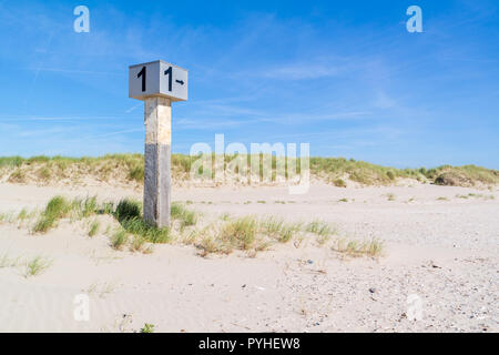 Marked beach pole with number 1 in sand on dune with marram grass on Kennemerstrand beach in IJmuiden, Noord-Holland, Netherlands