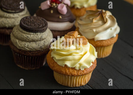 Assorted luxury decadent decorated cup cakes close up with selective focus isolated on rustic black background Stock Photo