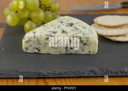 Blue cheese wedge on slate board close up with defocused green grapes and crackers in background Stock Photo