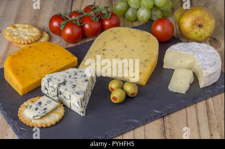 Cheese board with three cheeses, gouda with pimento, gouda with cumin seeds and roquefort blue cheese  and camembert close up on rustic wooden backgro Stock Photo