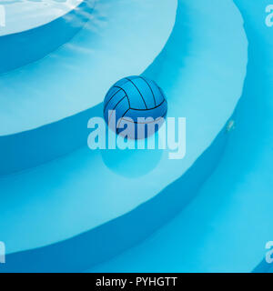 Square image of blue ball swimming alone on water surface in private pool. Stairs are visible through clean water with reflected surroundings. Summer  Stock Photo