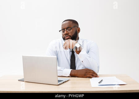 Irritated dark skinned young male enterpreneur being on working place feels very stressed and angry as cannot manage to do all work, surrounded with modern gadgets, looks in displeasure away Stock Photo