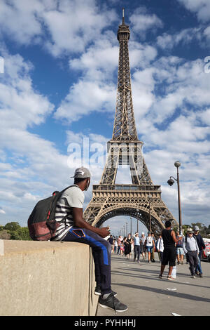 Paris, Ile-de-France, France - passers-by and a young African man on the Pont d'Iéna bridge, in the background the Eiffel Tower - the main landmark of the French capital. Stock Photo
