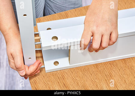 A furniture assembler connects parts of a wooden table, cam bolt fixings from one side and dowel pins from another side are inserted into holes on the Stock Photo