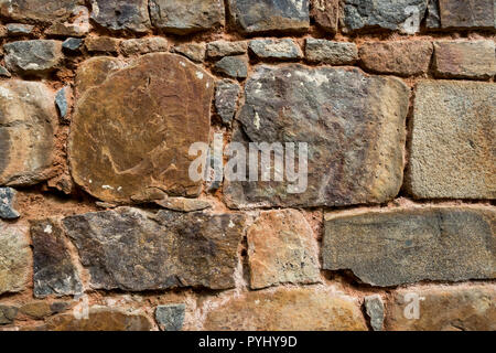 Background rock wall. A fragment of the old wall made of stones of various sizes connected with mortar. Stock Photo