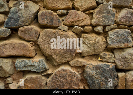 Background rock wall. A fragment of the old wall made of stones of various sizes connected with mortar. Stock Photo