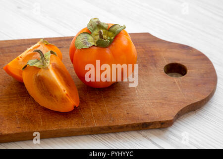 Fresh persimmon on a chopping board on white wooden background, side view. Close-up. Stock Photo
