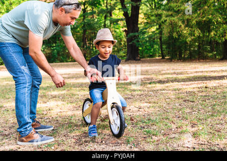 Father teaching his son to ride wooden bike in park Stock Photo