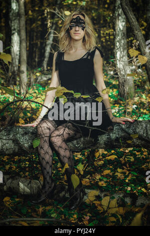 A young kind witch in a black dress with a black mask in a mystical forest in various poses. Art processing Stock Photo