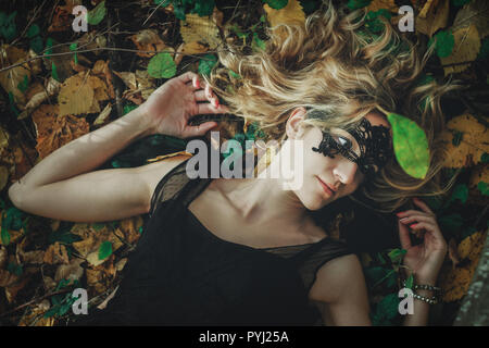A young kind witch in a black dress with a black mask in a mystical forest in various poses. Art processing Stock Photo