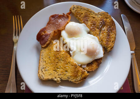 Lunch open sandwich of two poached eggs on  toasted multigrain bread topped with grilled smoked bacon Stock Photo