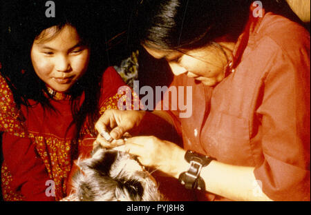 March 1974 - At the village of Ambler, an Eskimo woman teaches a young girl the art of sewing caribou skin into winter mukluks Stock Photo