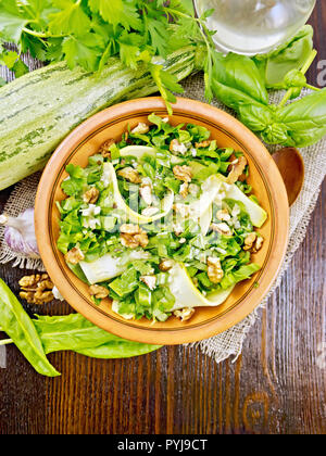 Salad of young zucchini, sorrel, garlic and nuts, seasoned vegetable oil in a plate on napkin of sackcloth on wooden board background from above Stock Photo