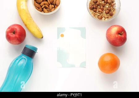 Attributes of a healthy lifestyle: food, sports and athlete's equipment on white background with note. Flat view with copy space. Eco bottle, nuts, oa Stock Photo