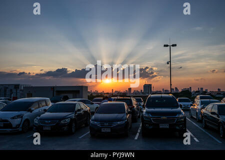 The sun is setting on twilight dramatic sky, over cars, on top roof carpark in Bangkok. Thailand. 27/10/18 Stock Photo