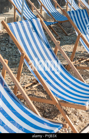 Blue and white wooden Deckchairs on a sandy beach opened. ready for sunbathing. Stock Photo