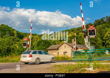 A white passenger car crossing a railroad crossing with barriers. Semaphores in front of the railway crossing. Warning signaling on railway in the Cze Stock Photo