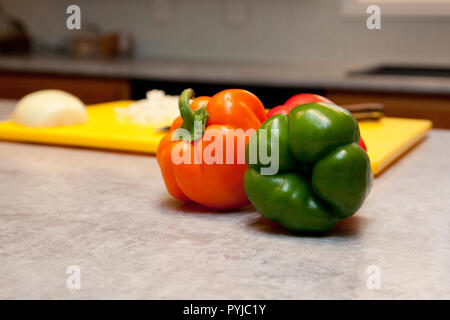 Red and green bell peppers next to a cutting board in the kitchen with copy space Stock Photo