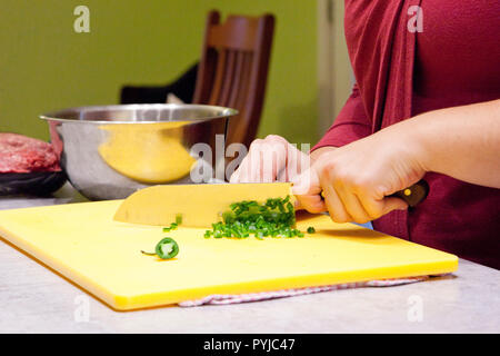 A sharp kitchen knife slicing shallots or green onions on a cutting board Stock Photo